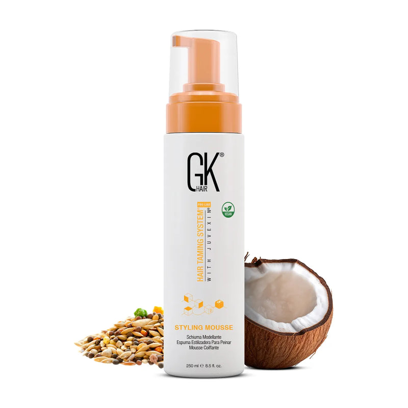 GK Hair Styling Mousse Pro 250 ml white pump bottle, front view with a halved coconut and mixed seeds beside it