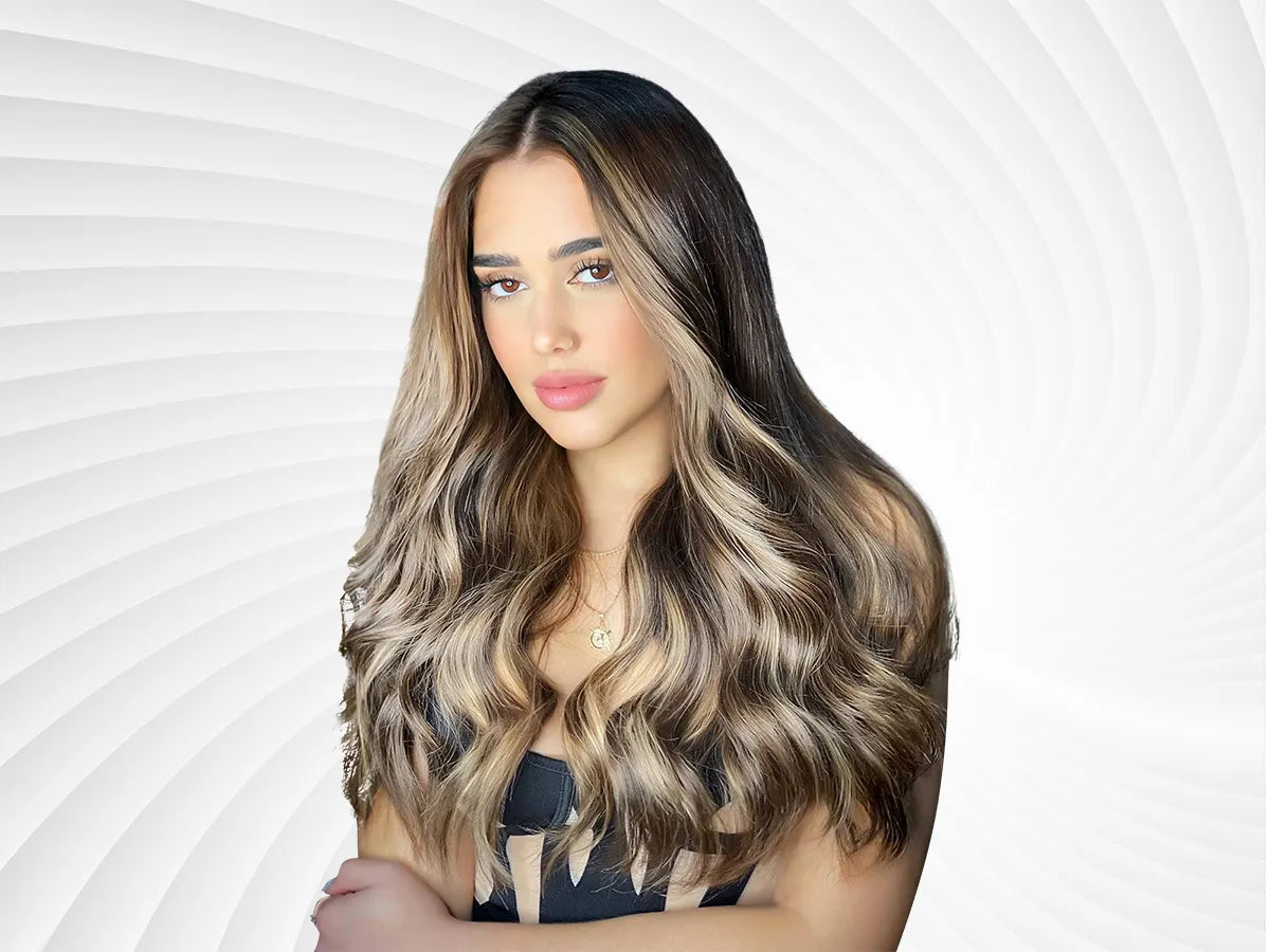 A person with long, wavy hair featuring blonde highlights, wearing a black tank top, poses against a soft, spiral background.
