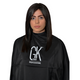 Dark-haired woman wearing the black GK Hair Professional salon cape, white logo printed across the chest